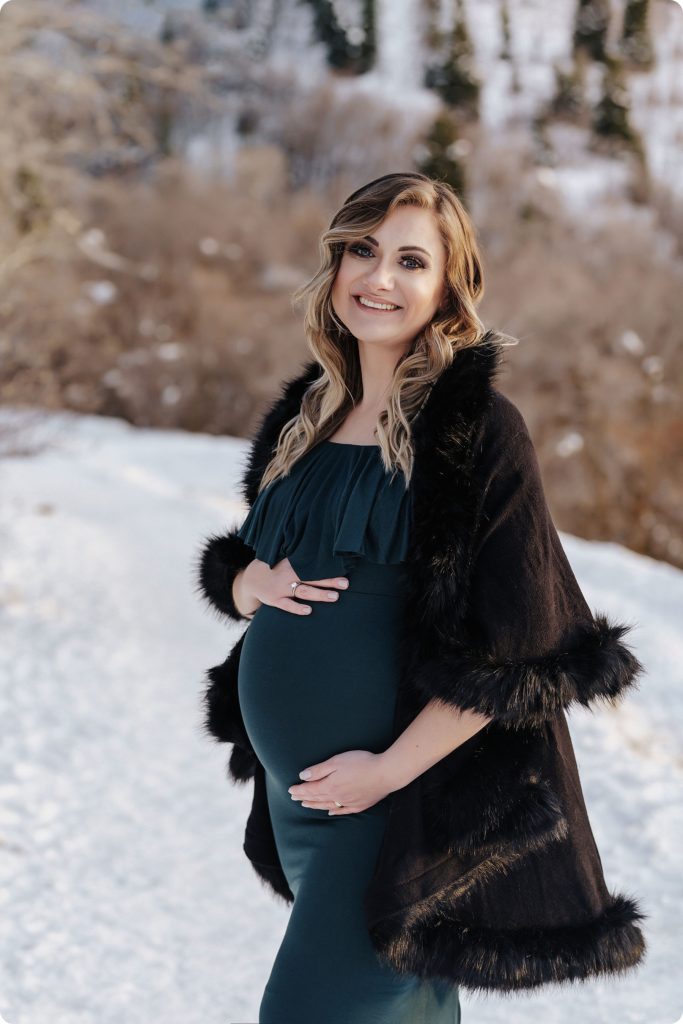 mother to be in green gown holds belly with brown jacket