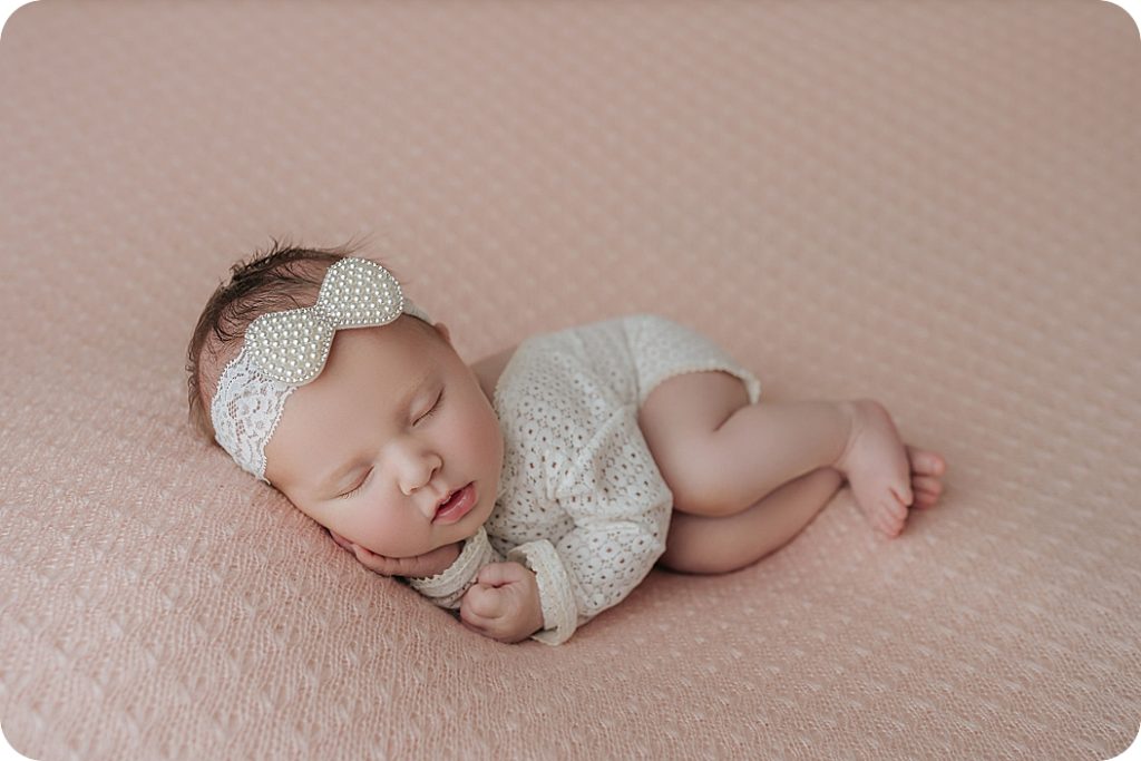baby girl in white outfit poses on pink spread