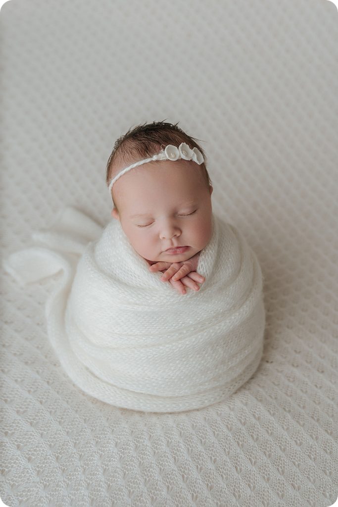 newborn baby girl in white wrap on bed
