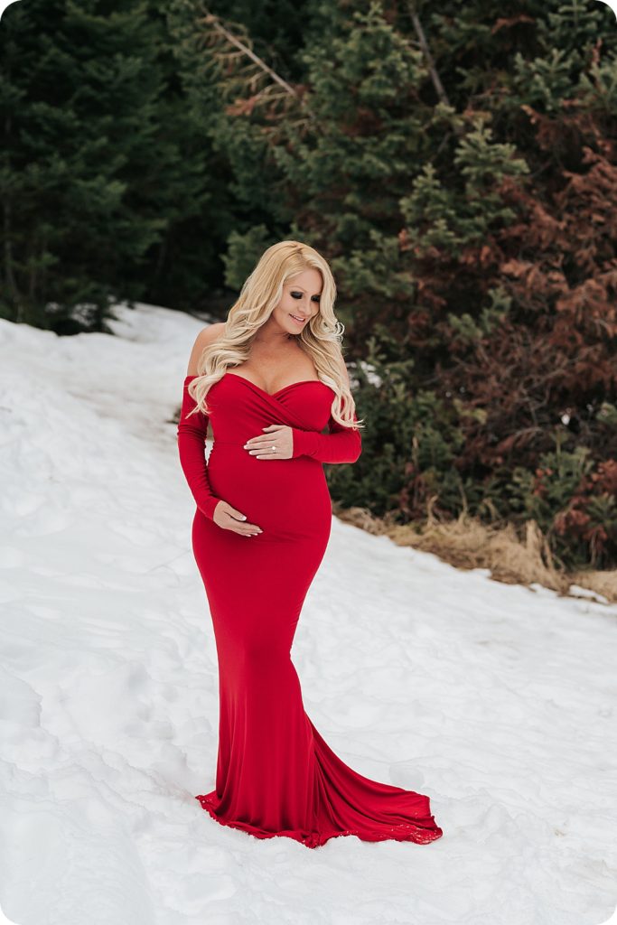mother in red maternity gown poses in snow in Salt Lake City