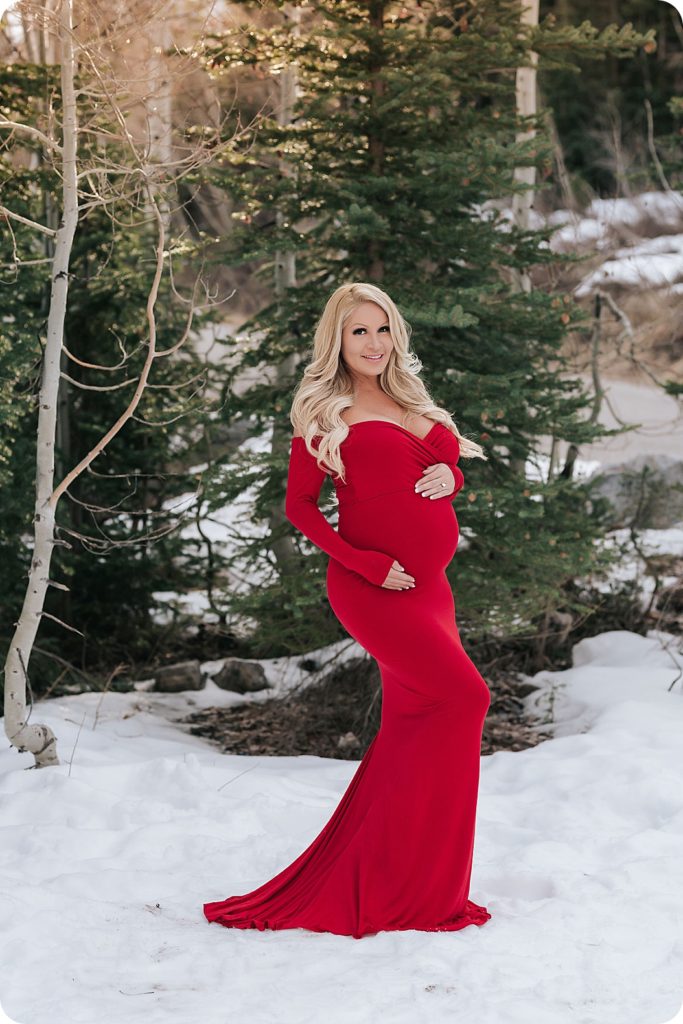 mother-to-be poses in red gown against snow on mountain
