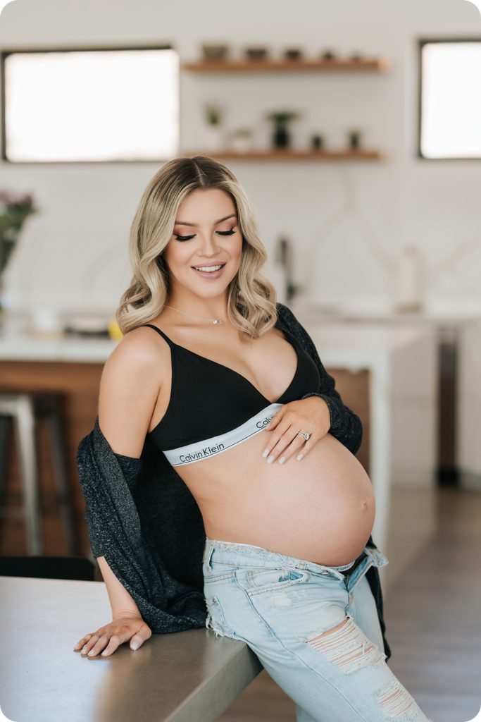 expectant mother holds belly during maternity portraits in kitchen 