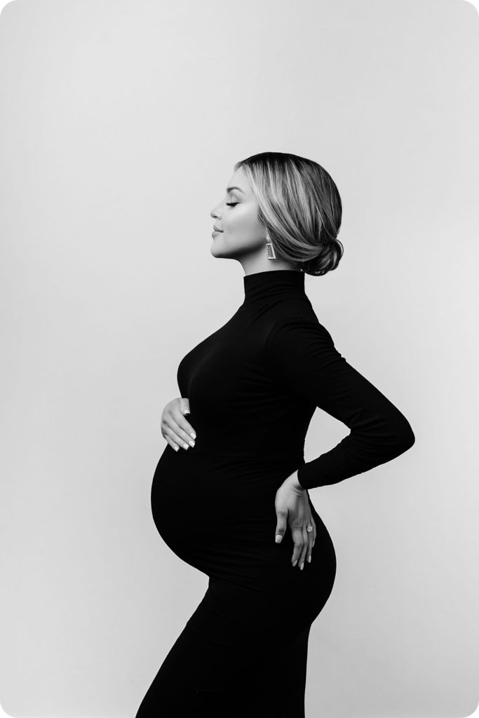 mom in sleek black gown holds baby bump with hair in a bun
