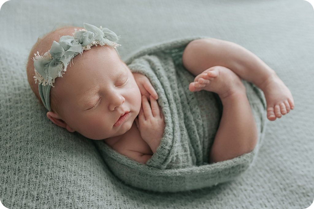 baby girl curls up in green wrap with floral headband photographed by Beka Price Photography