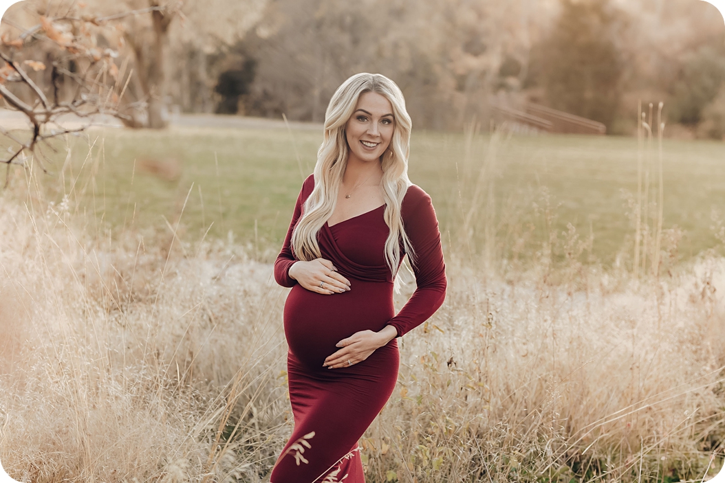 mom in cranberry maternity gown holds belly during maternity session with Beka Price Photography 