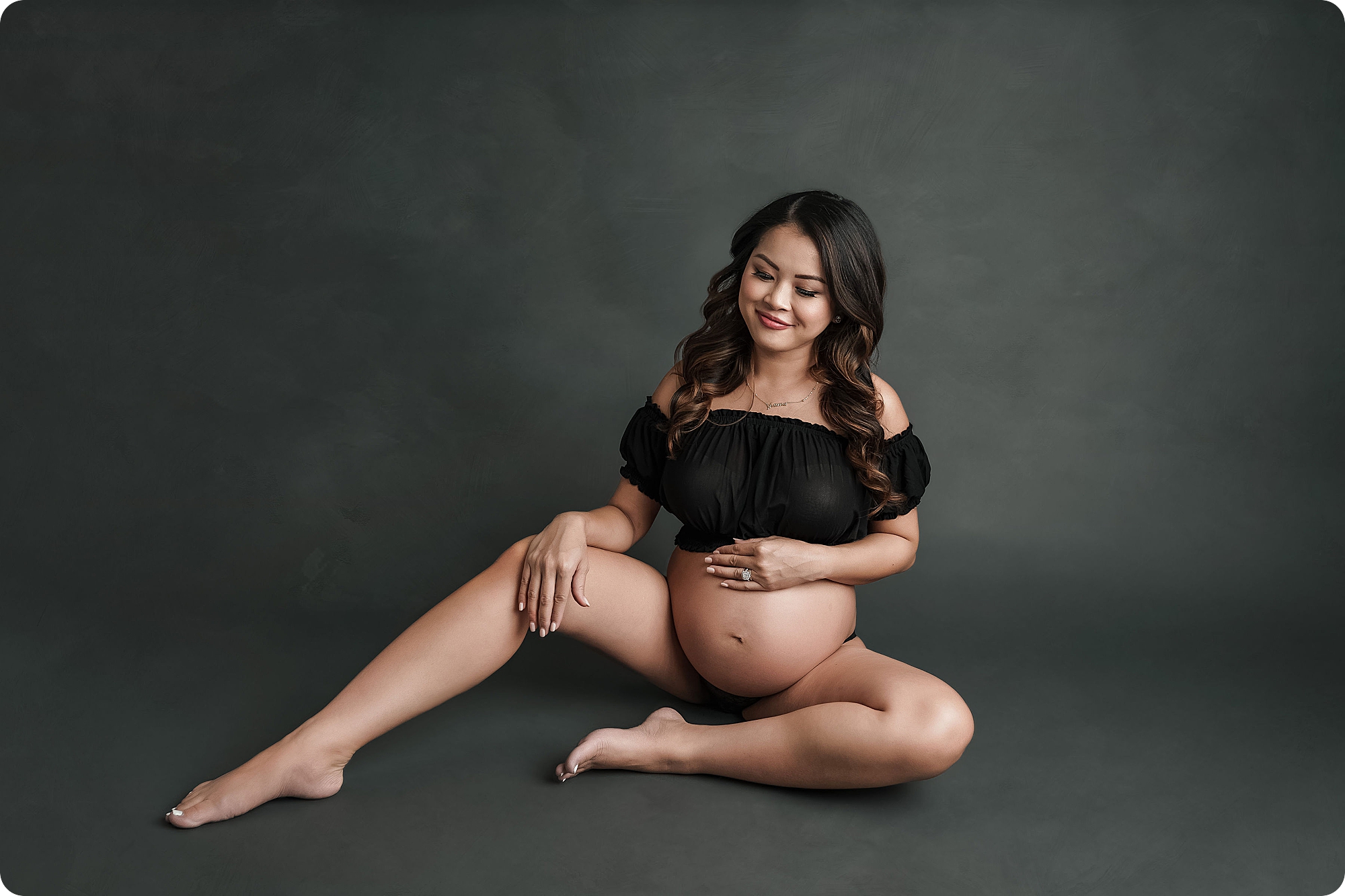 mom sits on floor and holds belly during glam maternity portrait session