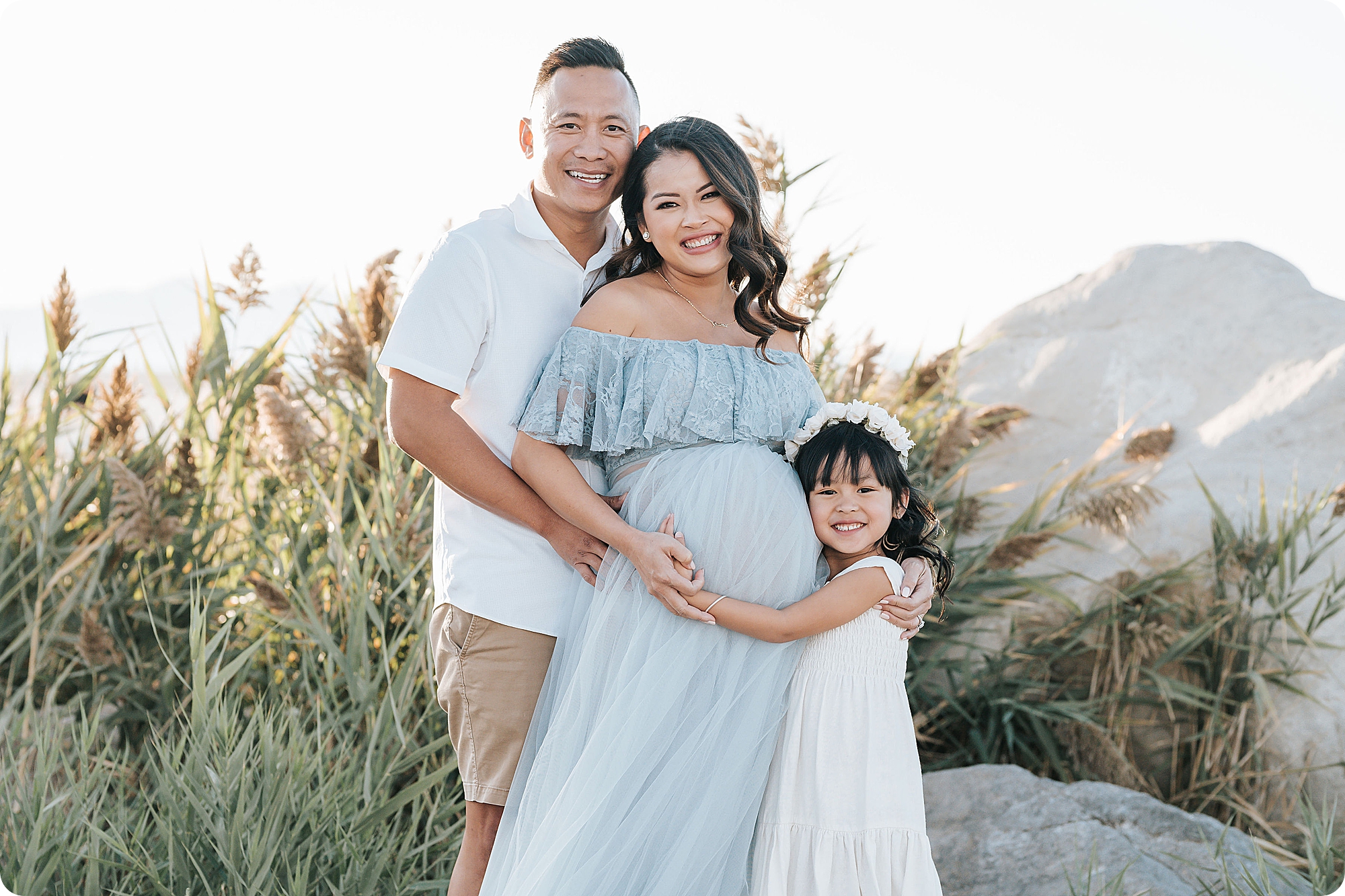 family of three poses during maternity session on beach