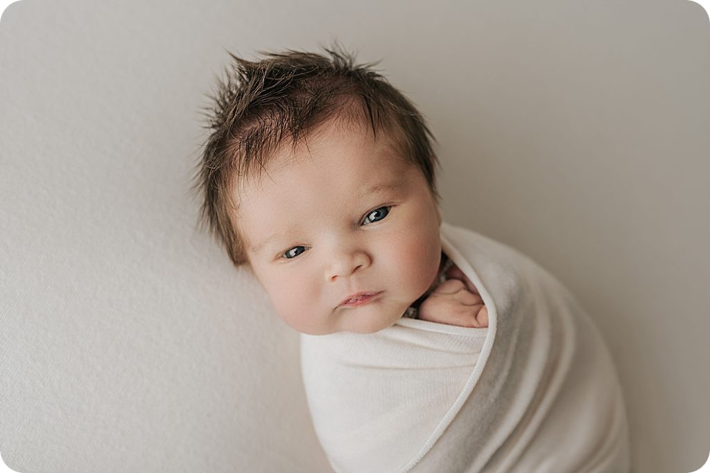baby in cream wrap looks at Utah newborn photographer