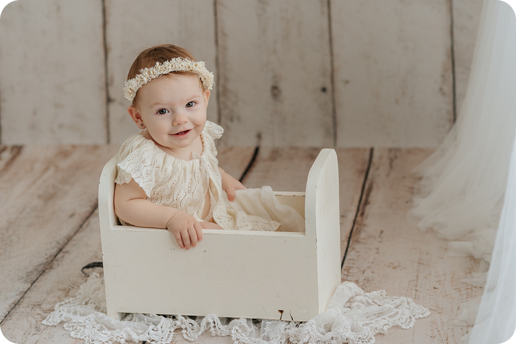 baby girl in white flower crown and dress smiles at Utah Photographer during milestone photos