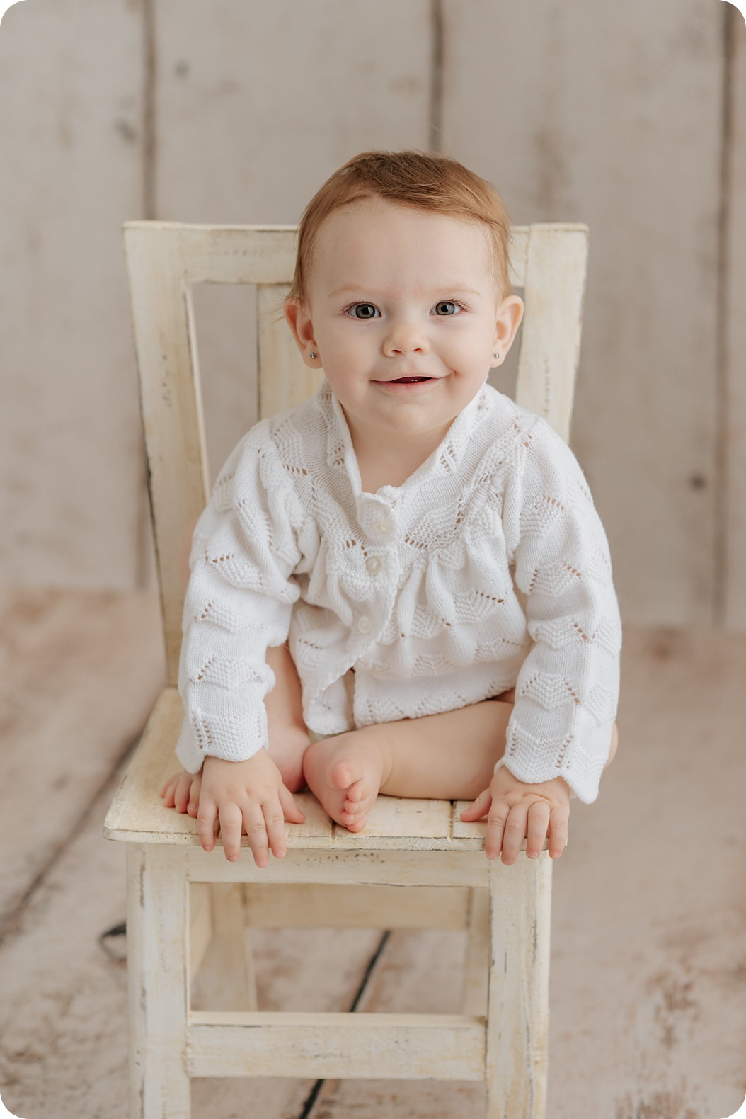 baby girl sits on rustic chair during classic first birthday milestone portraits