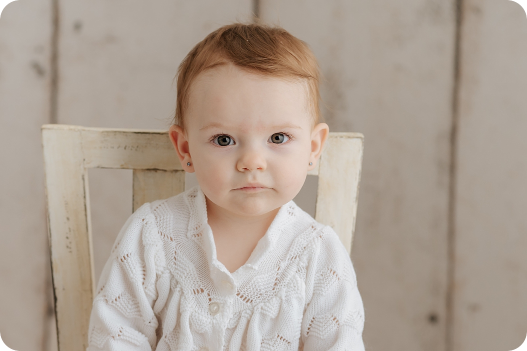 baby girl with red hair sits in rustic chair during studio portraits