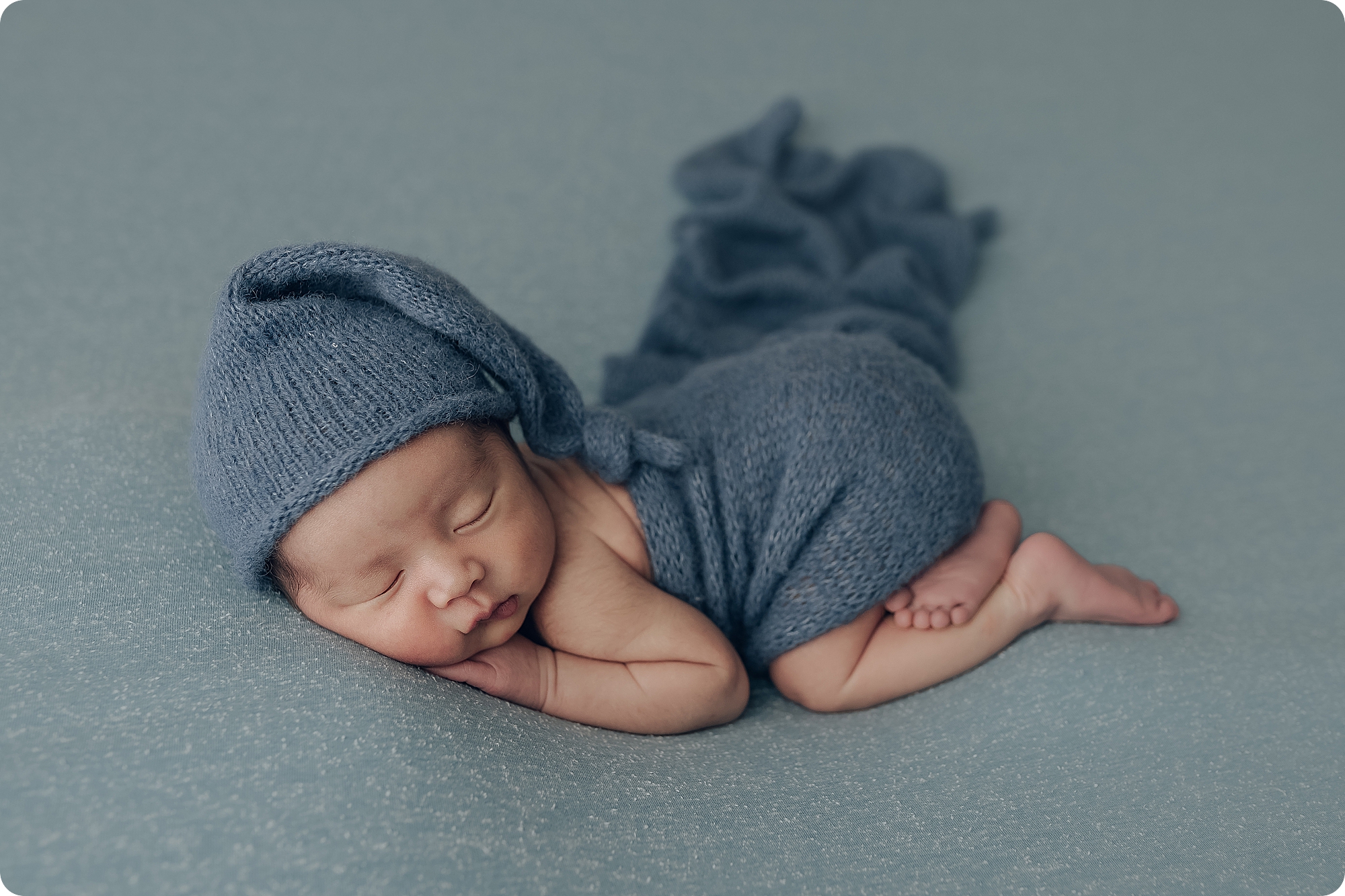 baby in blue knit cap sleeps during classic studio newborn session