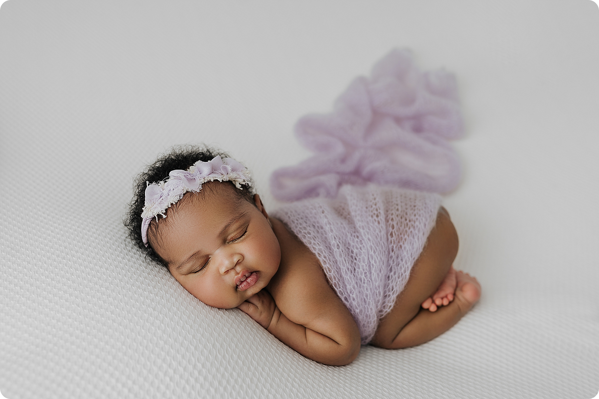 baby girl sleeps with lavender wrap and bow in her hair during UT studio session