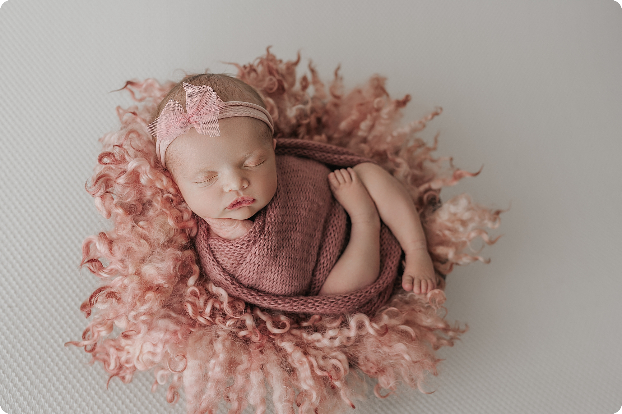 baby girl sleeps on pink floki with ribbon on head