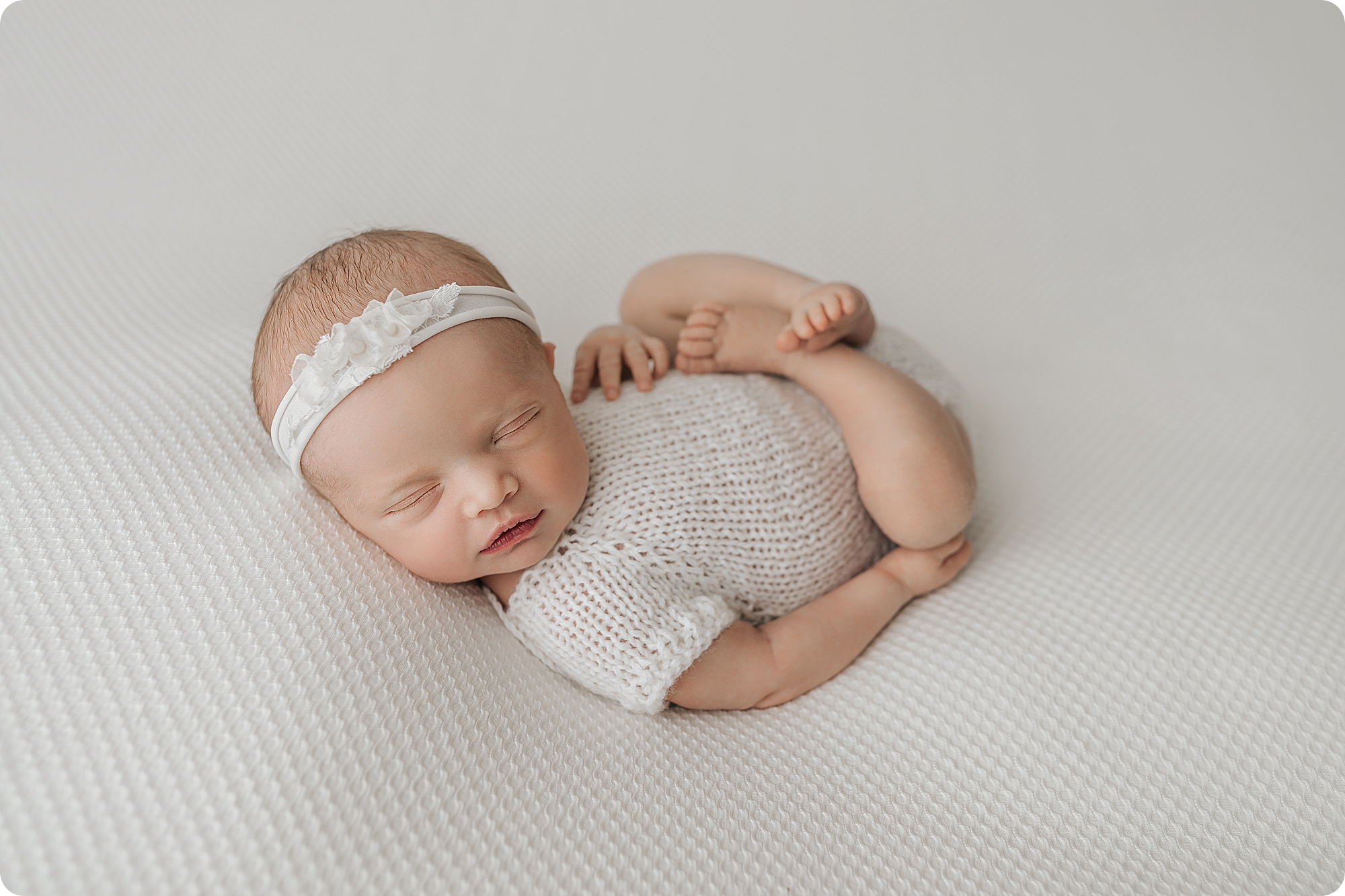 baby sleeps curled up in white knit outfit during cozy studio newborn portraits 