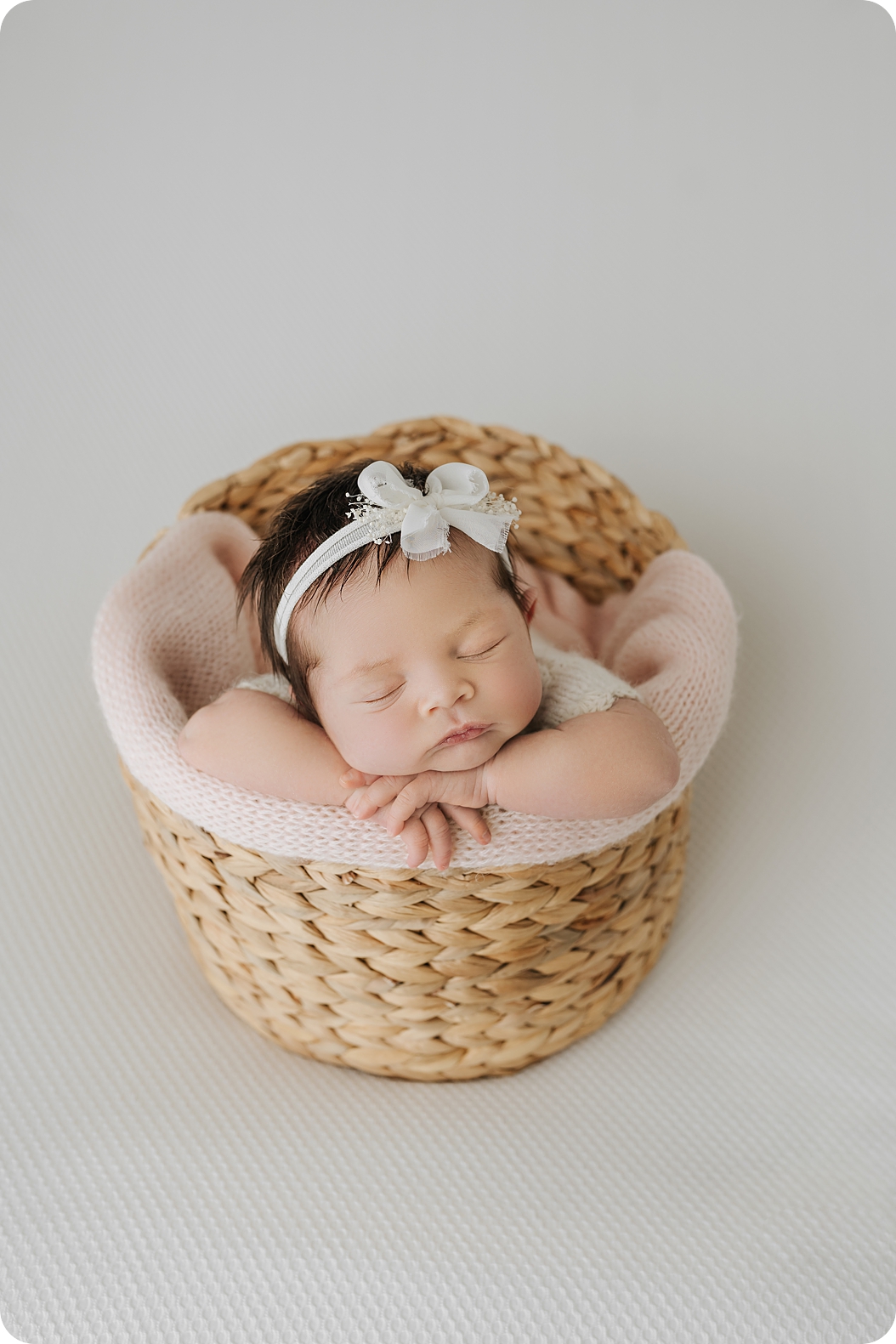 baby girl sleeps in basket with white headband during UT newborn photos
