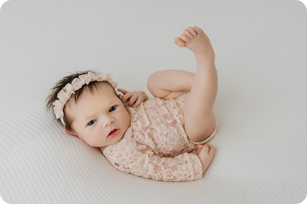 baby girl in lace romper lays on ivory backdrop during Utah newborn session with Beka Price Photography 
