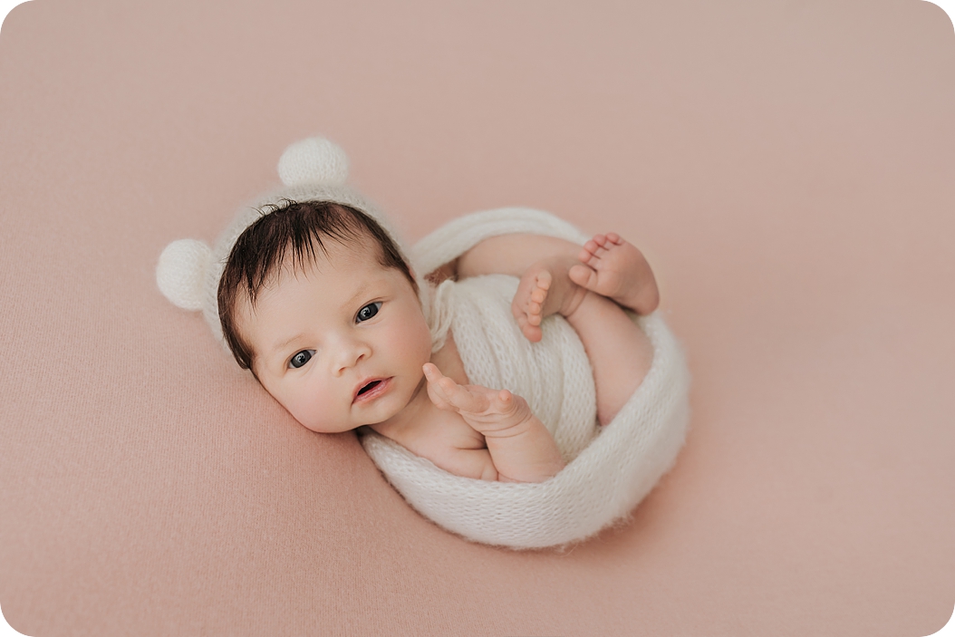 baby girl in ivory hat curls up during newborn session with Beka Price Photography 