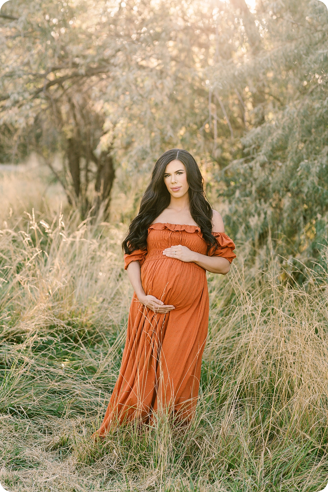 mom in orange gown holds belly during sunset maternity session in Holladay UT 