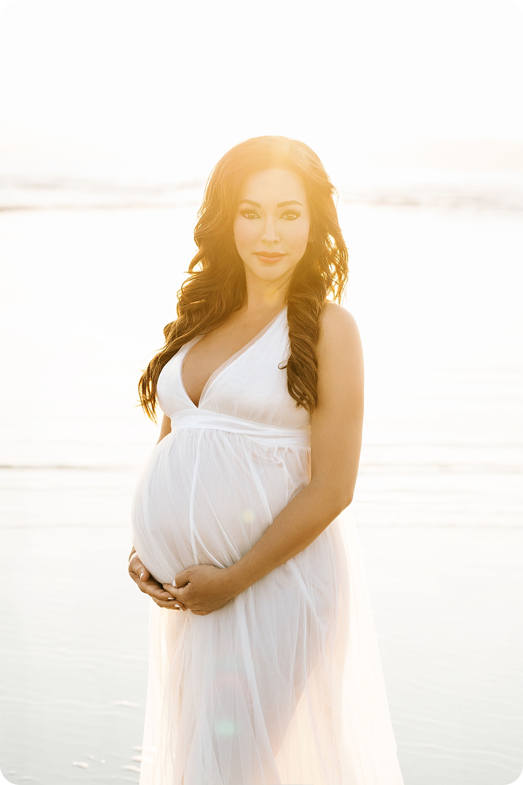 mother holds baby belly wearing all white gown during summer pregnancy photos