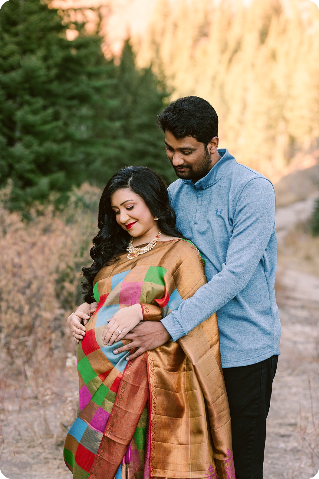 expecting mother in traditional Indian dress looks down at belly during maternity photos in Utah