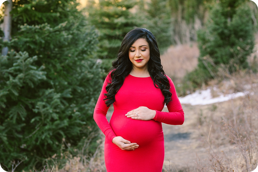 mother in red maternity gown holds baby belly during UT maternity photos