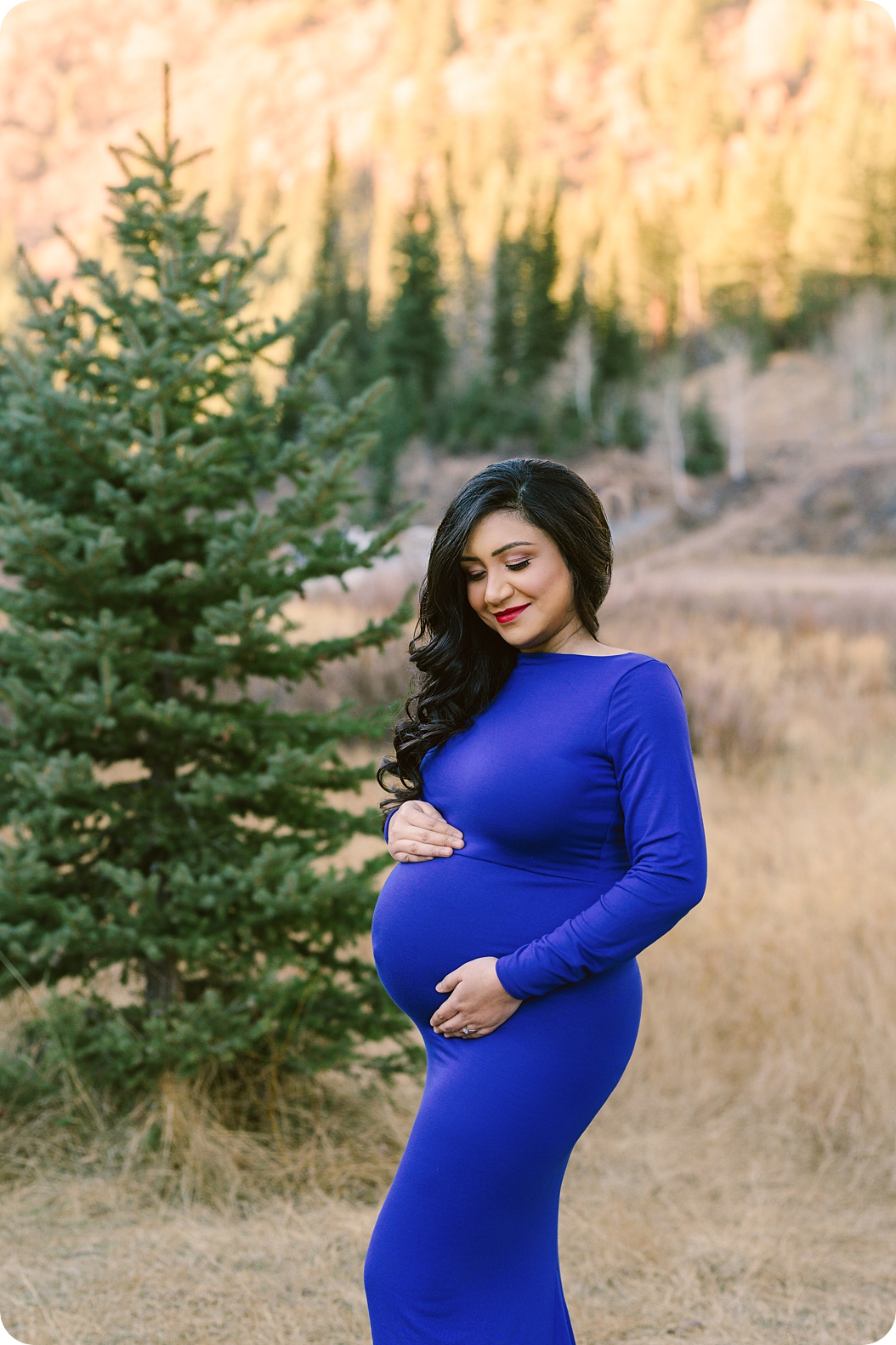 mom in dark blue gown holds baby belly during mountainside maternity photos