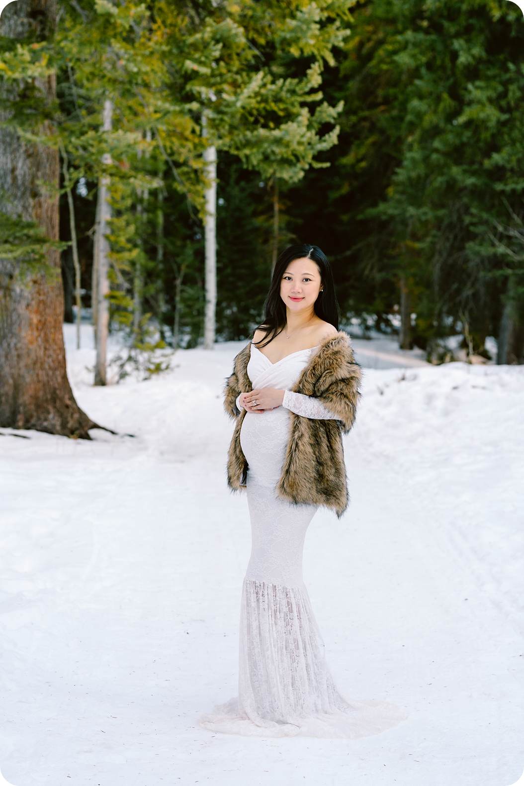 mom in white maternity gown folds hands on top of belly during Winter Maternity Portraits