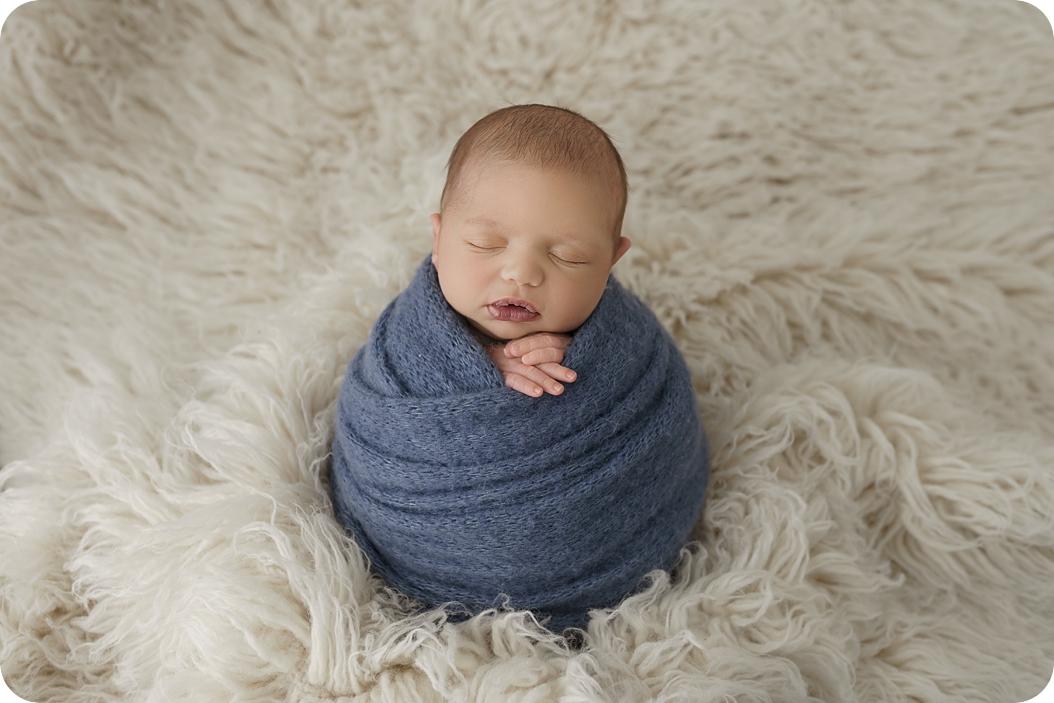 baby in blue wrap lays on ivory floki during newborn photos with Beka Price Photography