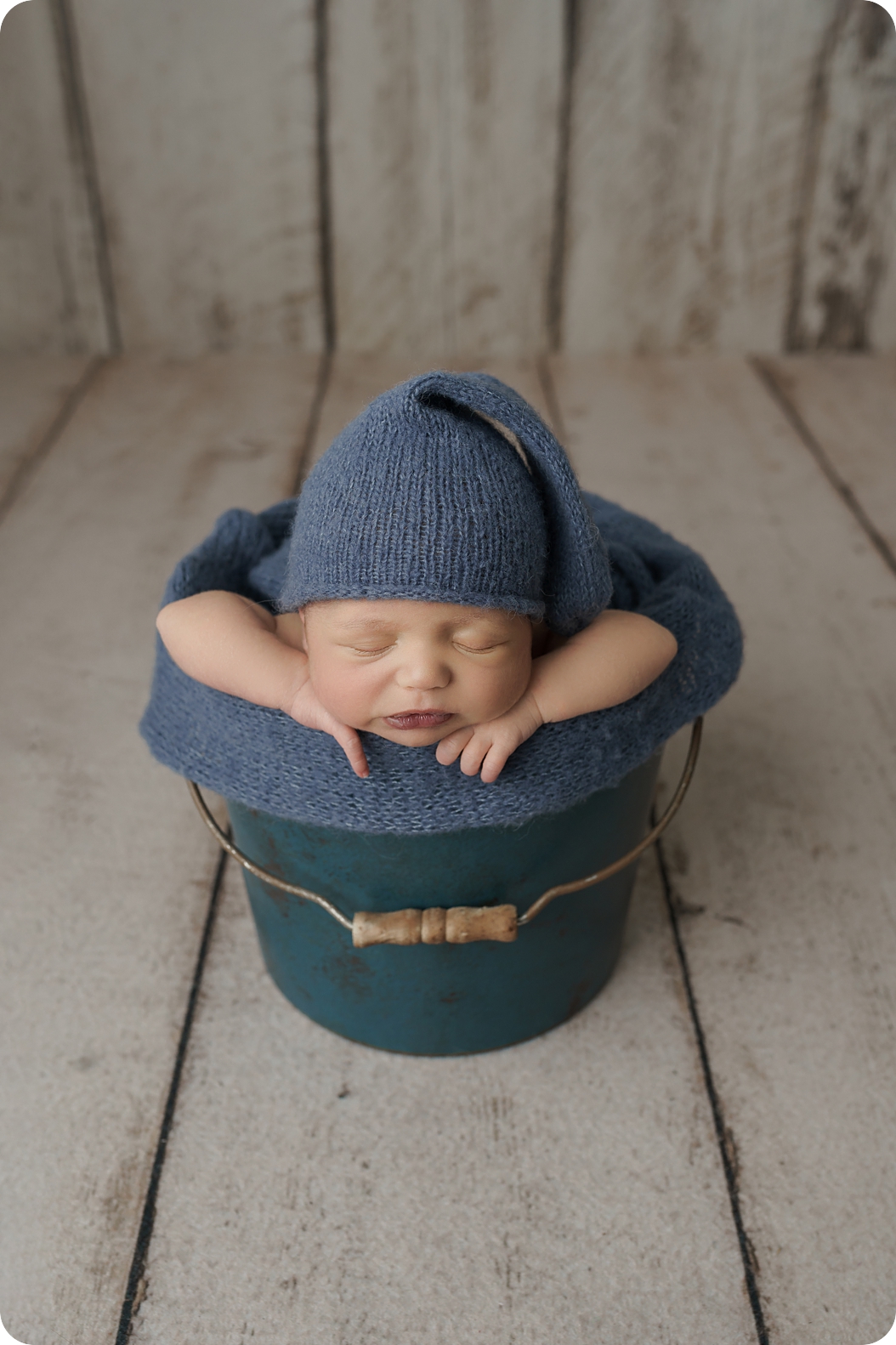 baby in blue knit cap sleeps in pail during Simple Studio Newborn Portraits