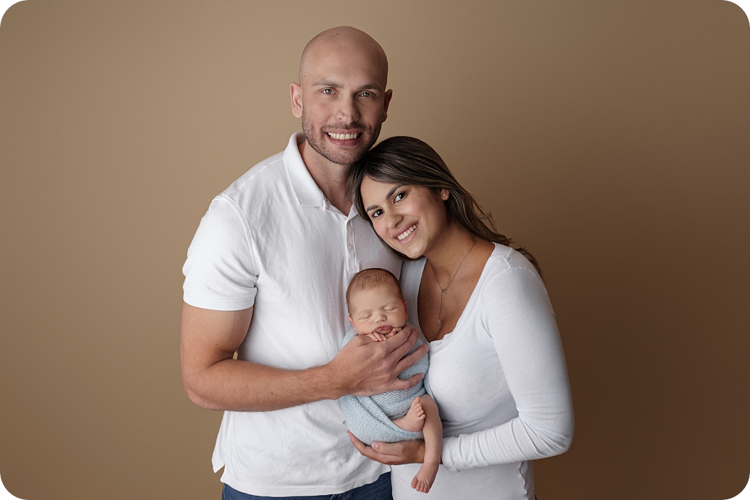 parents hold newborn baby boy in blue wrap during Simple Studio Newborn Portraits