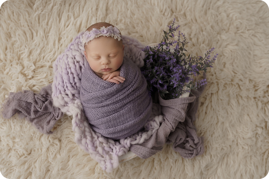baby girl sleeps on blanket during newborn session with pastel purple accents