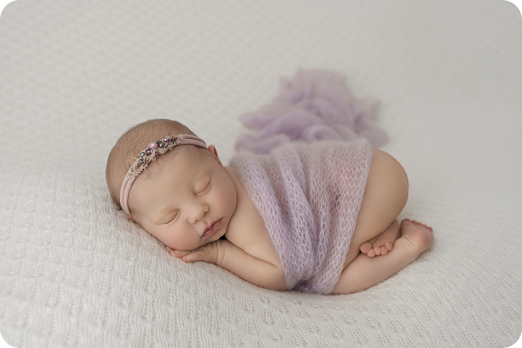 baby sleeps in purple wrap during newborn session with pastel purple accents