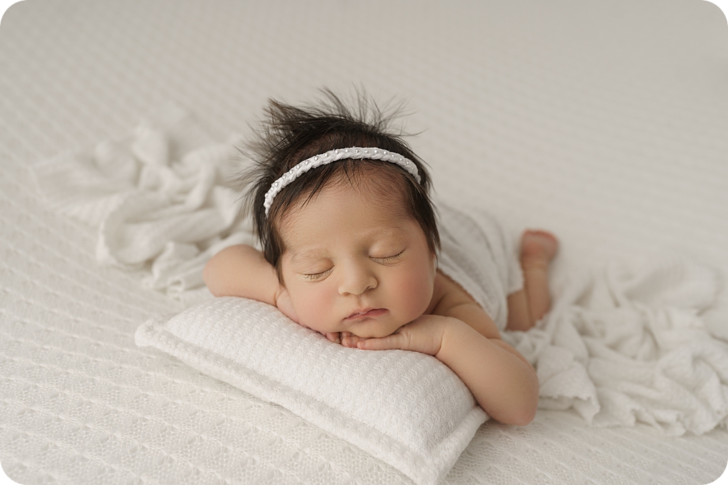 baby girl lays on pillow during studio newborn session in Utah