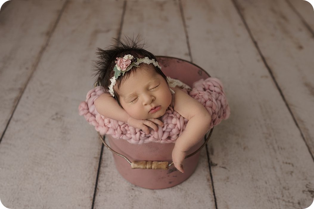 baby girl sleeps in pink bucket during newborn photos 