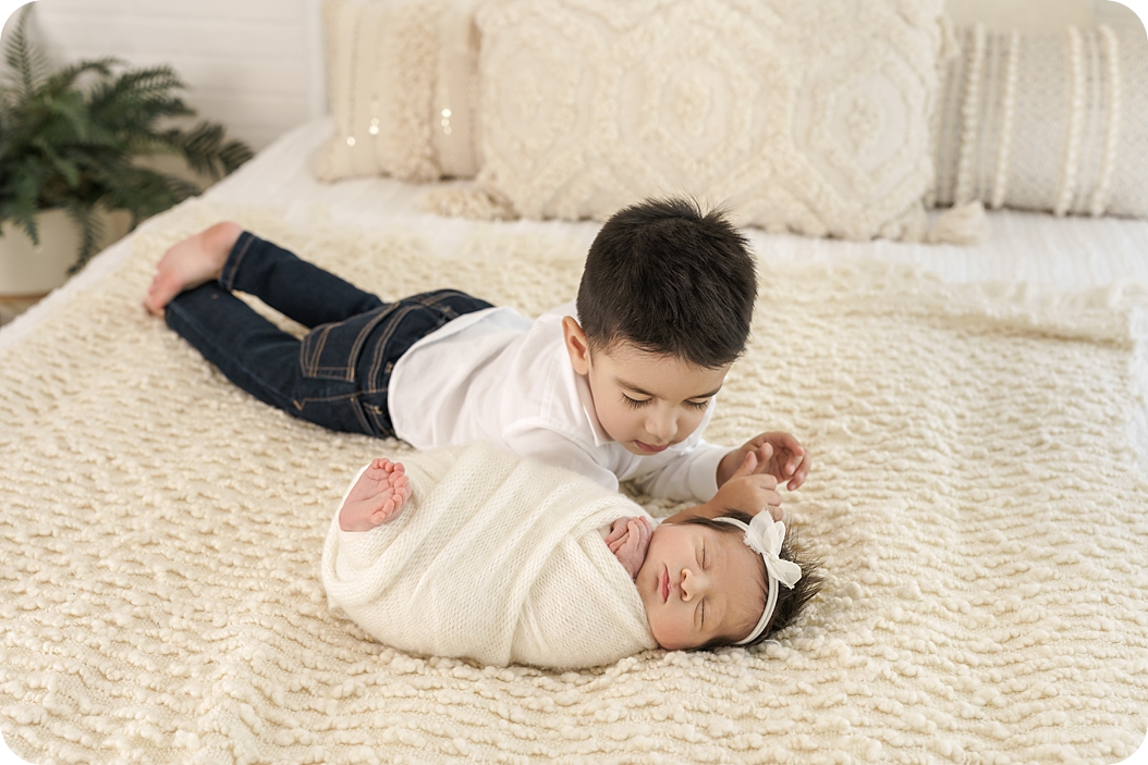big brother looks at baby sister during timeless newborn portraits in Utah studio