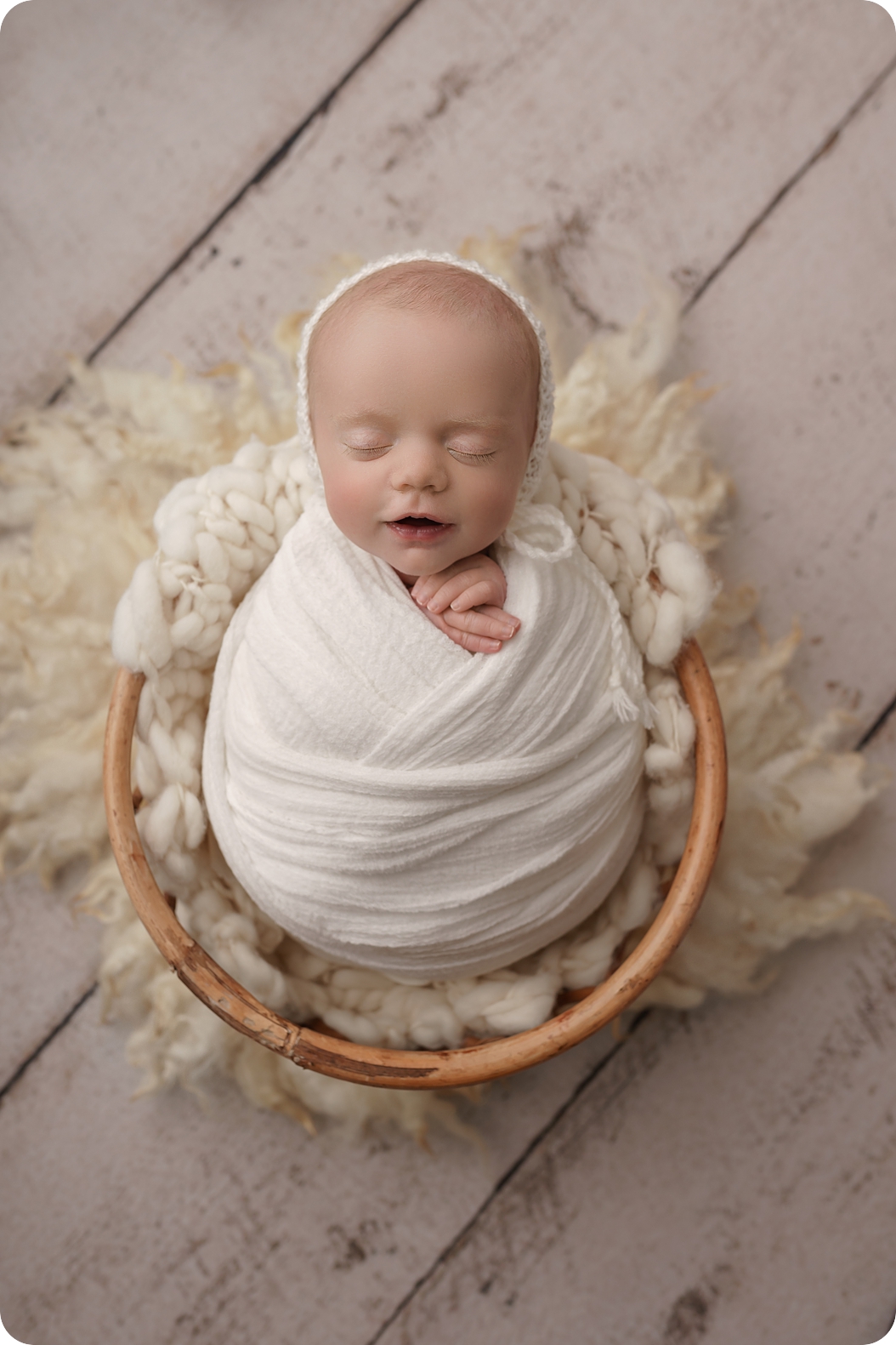 baby in ivory wrap sleeps in bucket during studio newborn portraits 
