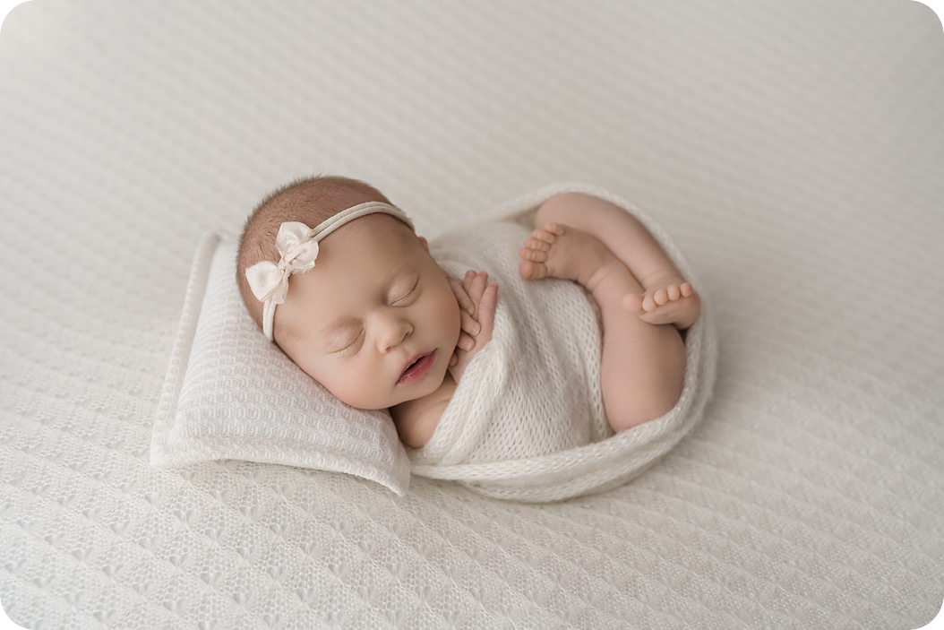 baby girl in white knit wrap sleeps curled up during studio newborn photos