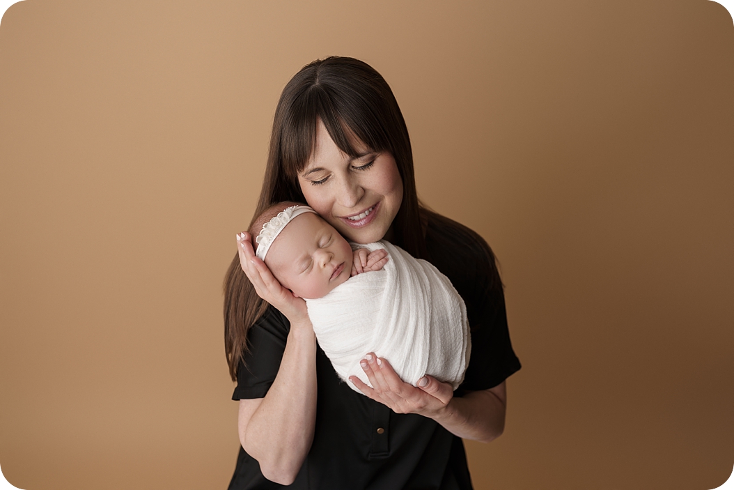 mom holds baby girl in white wrap during spring studio newborn session