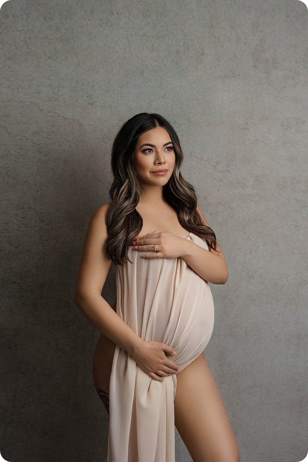 mother holds pale fabric against stomach during studio maternity portraits 