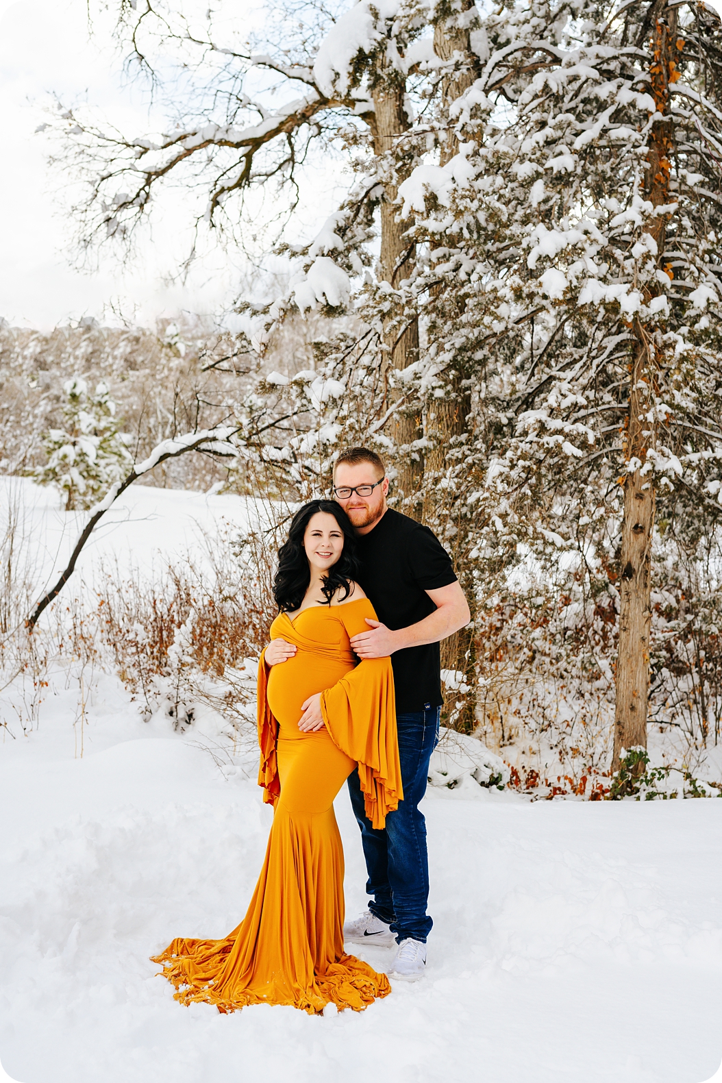 expecting parents pose during winter maternity photos in the snow 