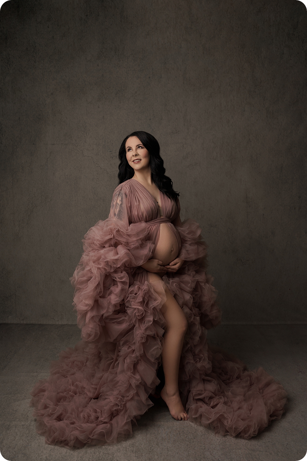 mother holds belly wearing mauve gown during studio maternity session 