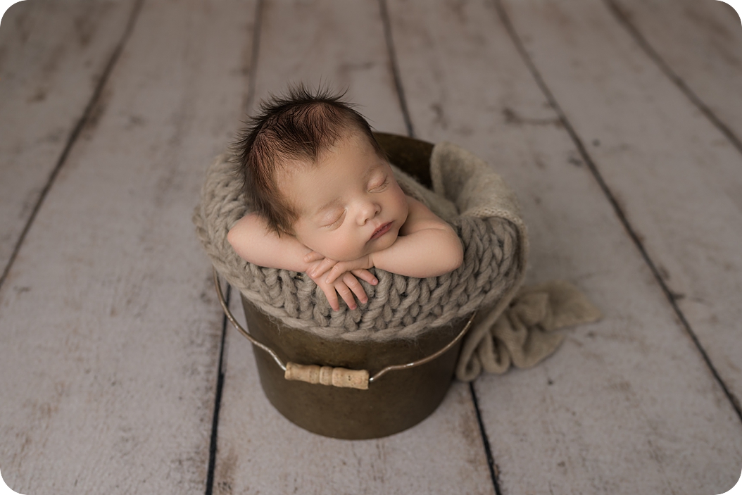 baby sleeps in brown pail during classic newborn portraits in studio