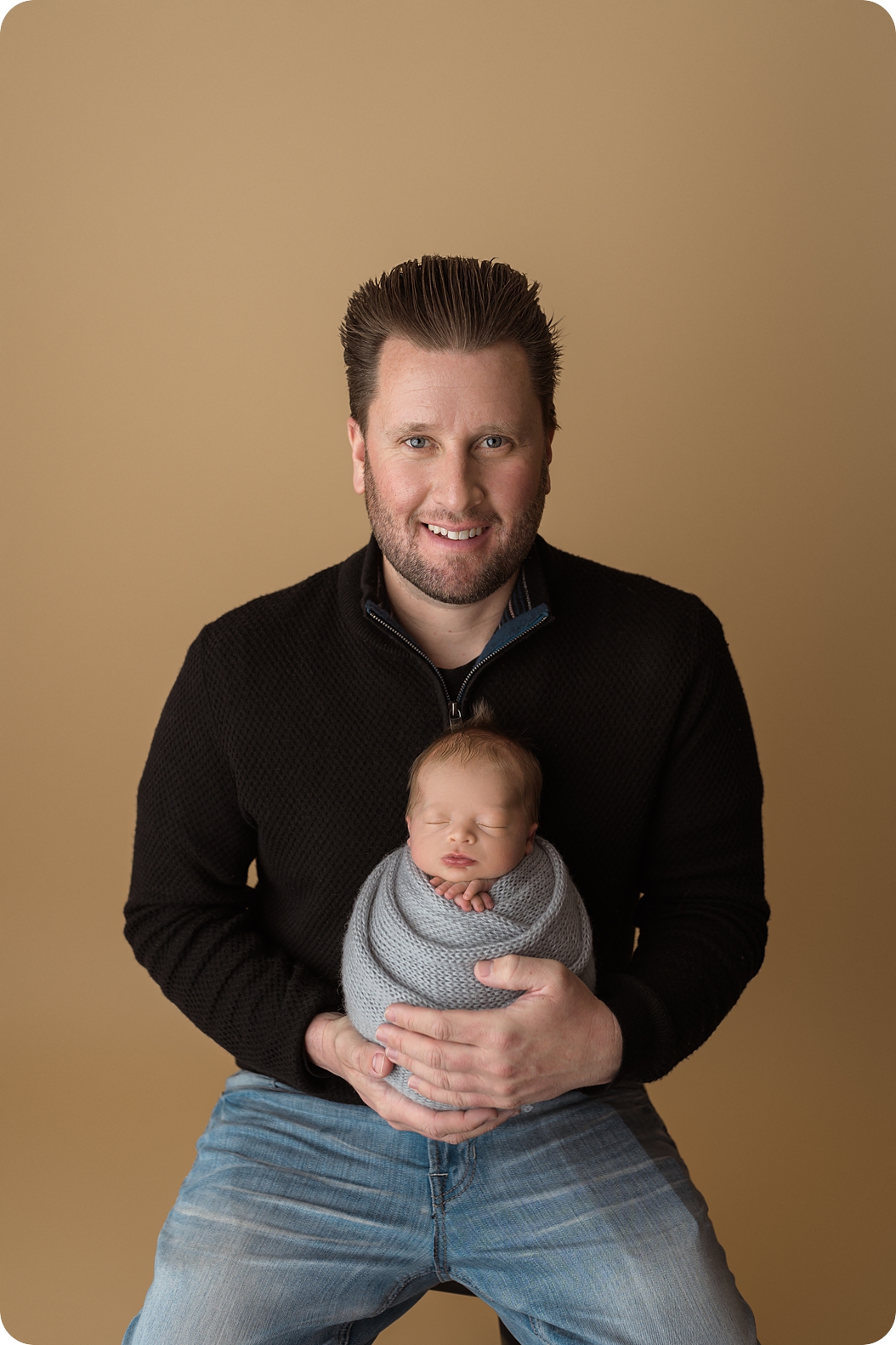dad holds son in lap during newborn photos in Utah