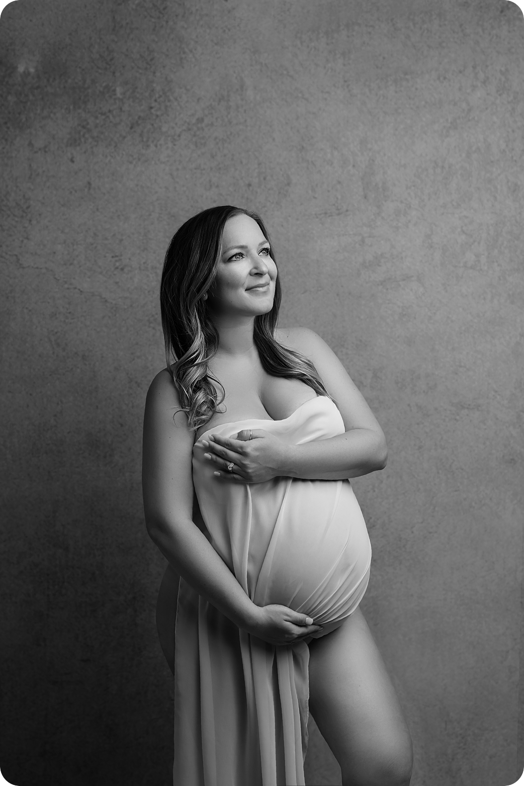 mom holds gauzy wrap around belly during classic studio maternity session 