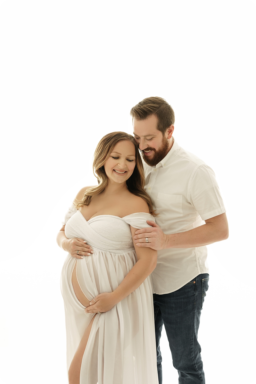 expecting parents pose together on white backdrop in Utah studio during classic studio maternity session 