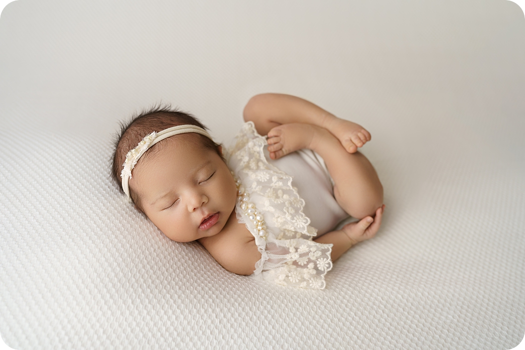 baby sleeps in ivory onesie with string of pearls during Utah newborn photos 