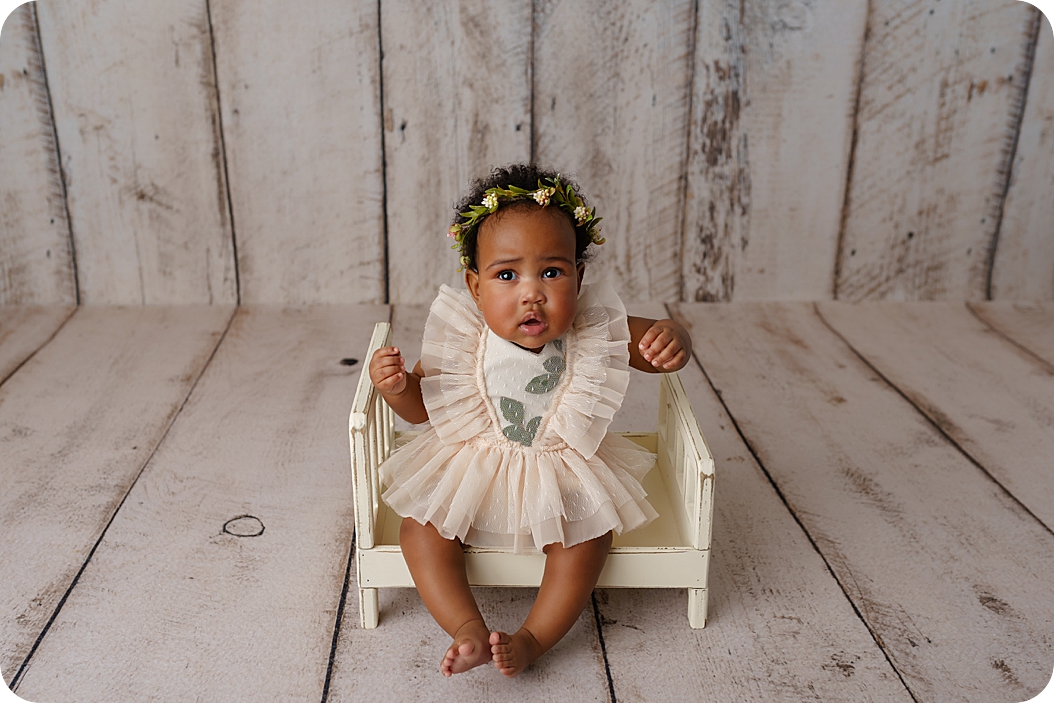baby girl in ivory dress laughs on little bed during studio portraits in Utah