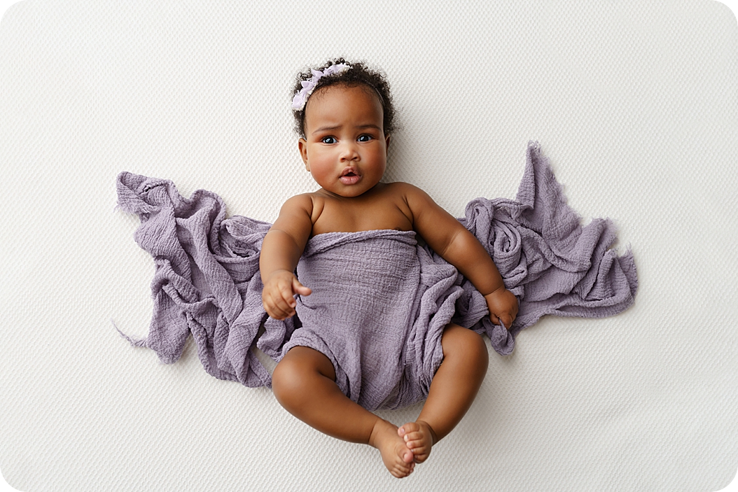 baby girl in purple wrap looks at camera during Studio Milestone Portraits