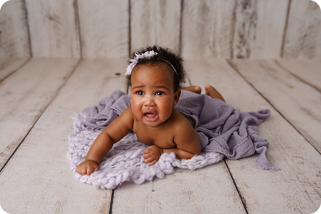 baby girl lays on purple wrap on wooden backdrop during Studio Milestone Portraits